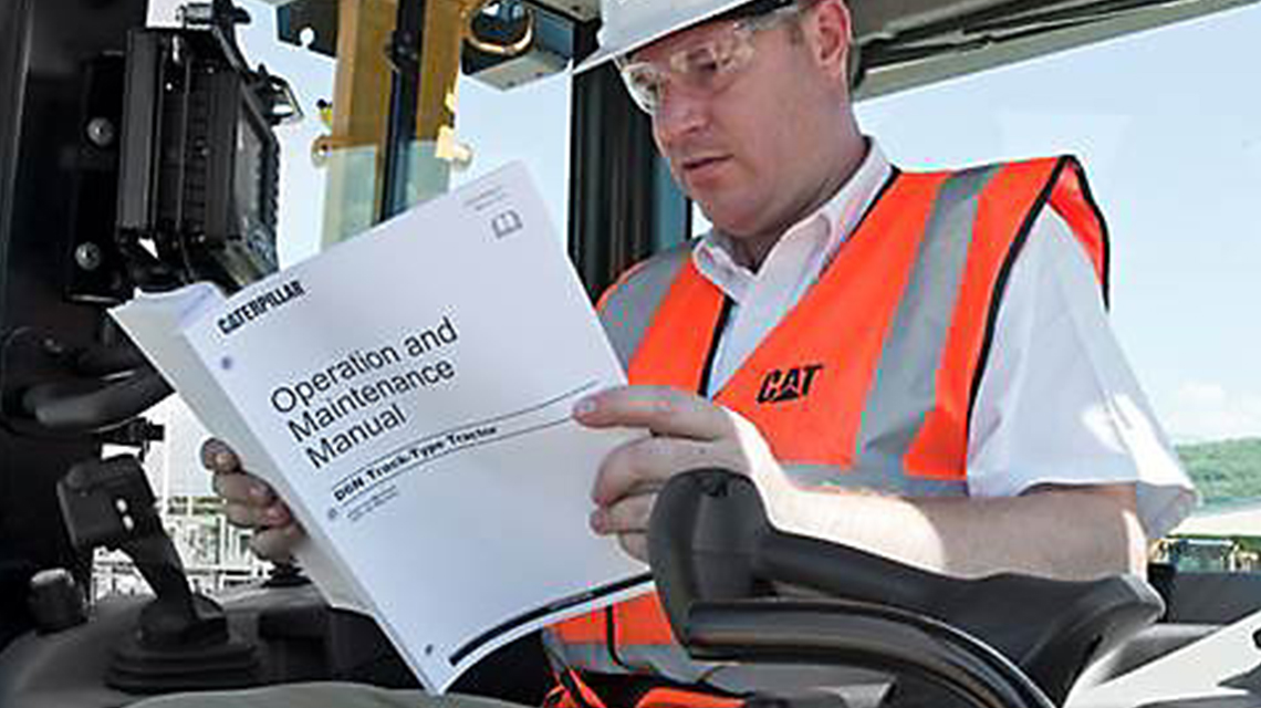 Technician wearing a high-visibility CAT safety vest seated in heavy equipment cab, reading a Caterpillar Operation and Maintenance Manual for D6N Track-Type Tractor.